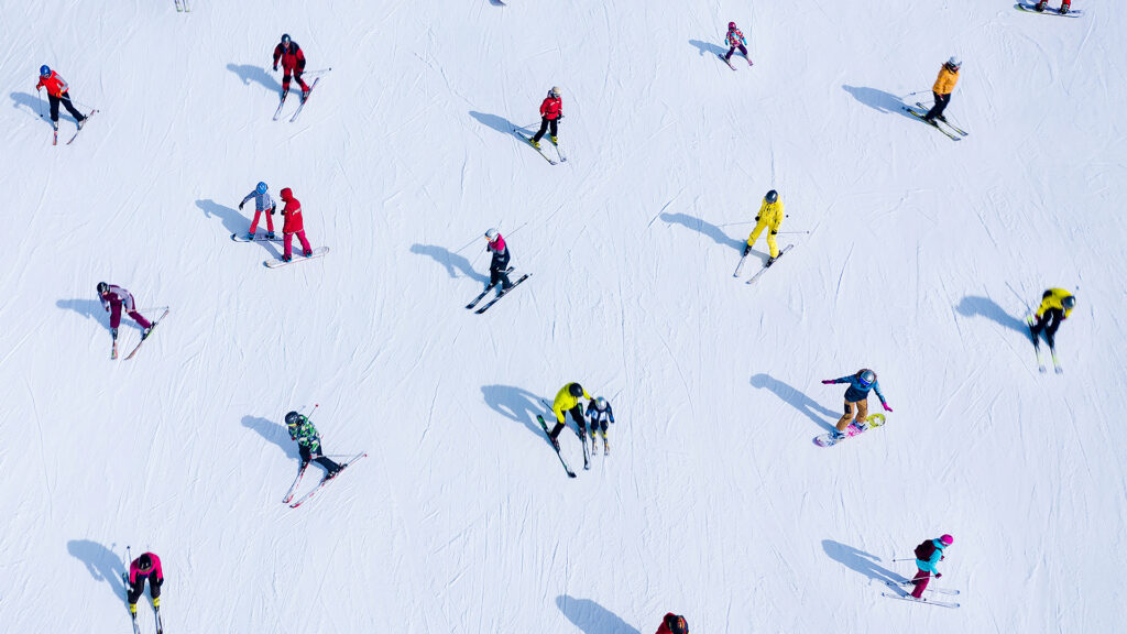 Ilmakuva lumisesta rinteestä täynnä hiihtäjiä eri värisissä hiihtoasuissa.