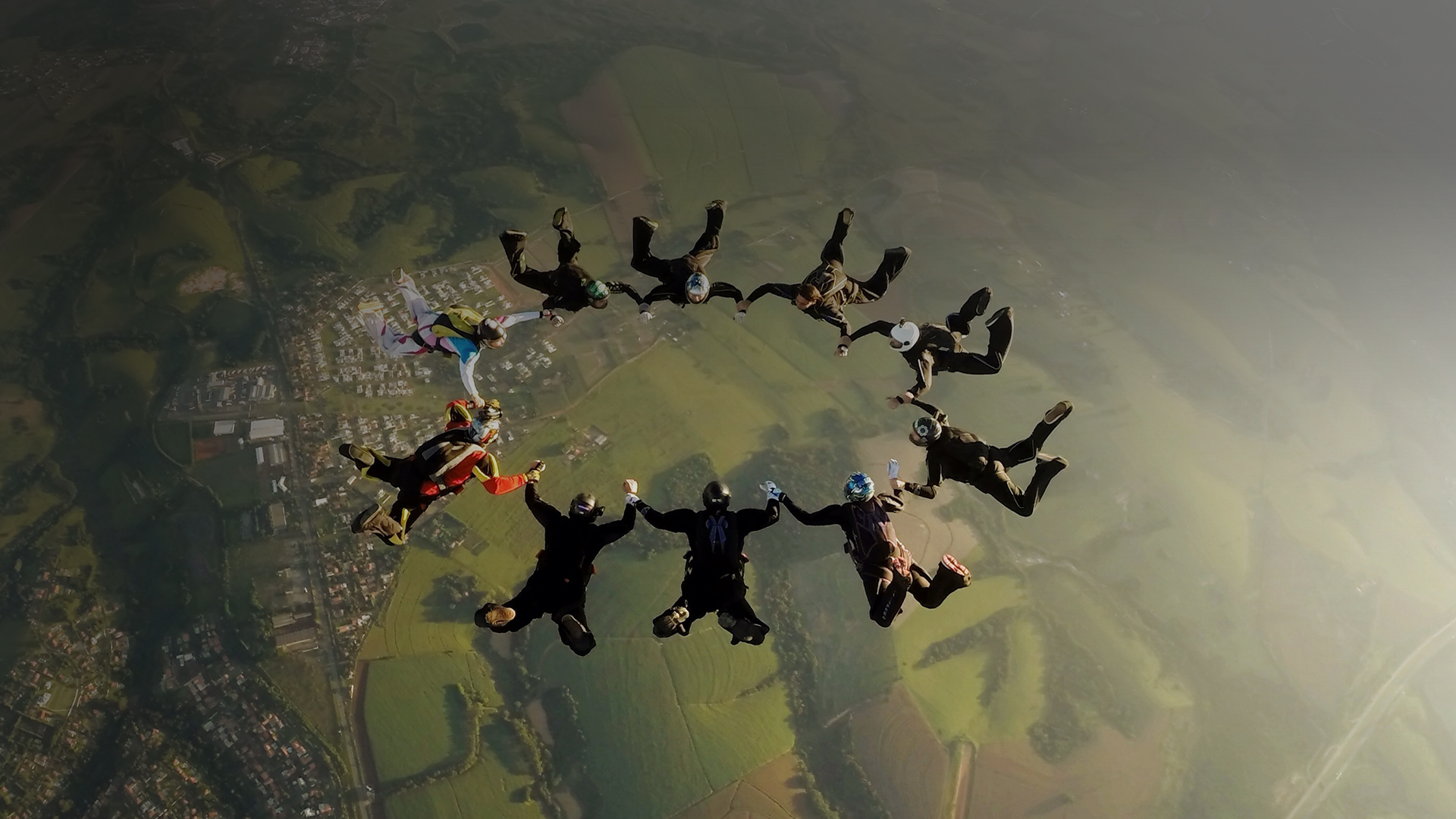 Ten people in a circular formation, flying in the air before their parachutes open.