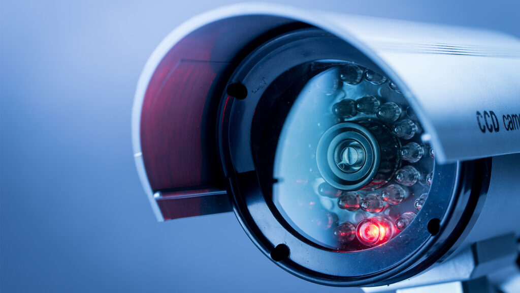 A close-up of a security camera lens with one bright red LED light burning.