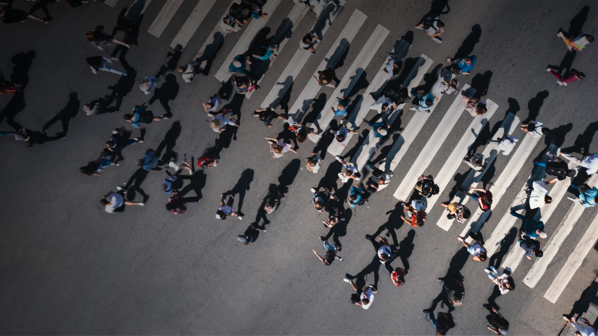 Mass of people walking on and beside a pedestrian crossing, seen from above.